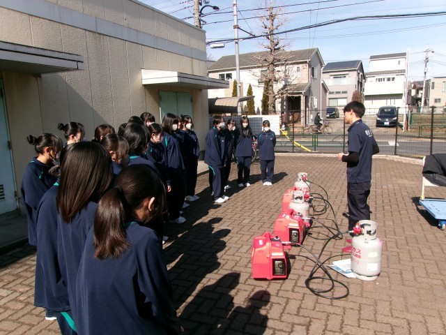 屋外で発電機の説明を聞く生徒たち